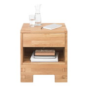 Houten nachtkastje met een lade en een open vak, gefotografeerd vanaf de voorkant, versierd met een karaf, een glas water en een notitieboekje.