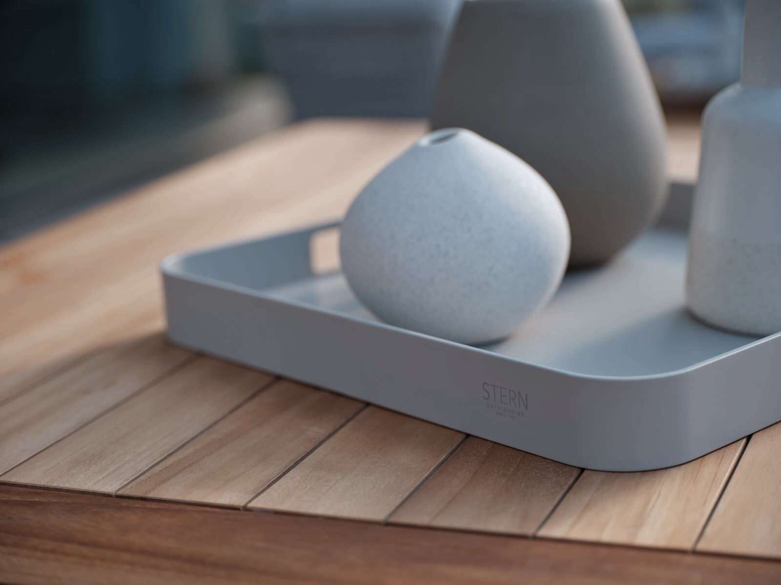 Graues Tablett mit abgerundeten Ecken, auf einem Holztisch stehend, mit drei dekorativen Vasen. Perspektive von schräg oben.