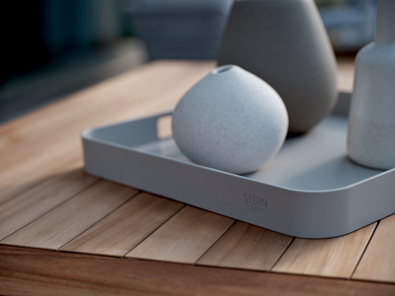 Graues Tablett mit abgerundeten Ecken, auf einem Holztisch stehend, mit drei dekorativen Vasen. Perspektive von schräg oben.