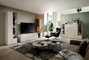 Moderne Vitrine im Wohnzimmer, links im Bild, mit Glasfronten und dekorativen Elementen, in einer eleganten, hellen Umgebung.