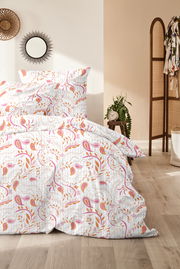 Bettwäsche-Set mit floralem Muster in Rosa und Orange, auf einem Bett in einem hellen Raum mit Holzboden und Dekorationen, aus der Perspektive von vorne.