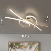 Moderne LED-Deckenleuchte in Weiß mit geschwungenen Lichtbändern, ca. 100 cm breit, 44 cm tief und 10 cm hoch, Ansicht schräg von unten an der Decke montiert.