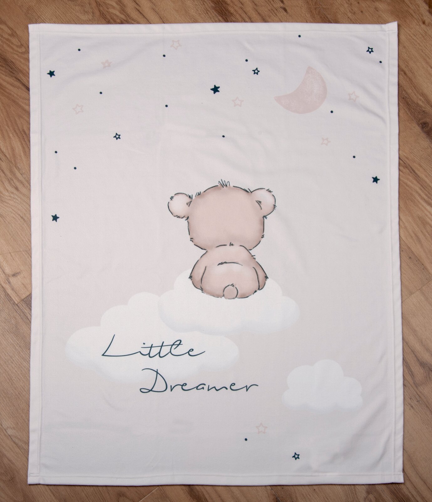 Weiche Decke mit einem niedlichen Bärenmotiv, der auf einer Wolke sitzt, umgeben von Sternen und dem Mond. Perspektive von oben.