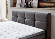 Graues Boxspringbett mit gepolstertem Kopfteil, seitliche Perspektive