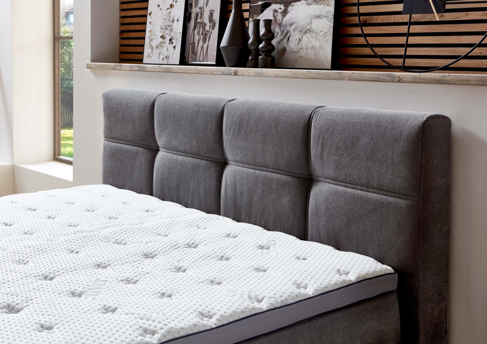 Graues Boxspringbett mit gepolstertem Kopfteil, seitliche Perspektive