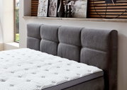 Graues Boxspringbett mit gepolstertem Kopfteil, seitliche Perspektive