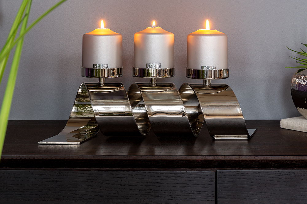 Moderner dreiflammiger Kerzenhalter aus Metall in wellenförmigem Design, frontal auf einem dunklen Tisch platziert.