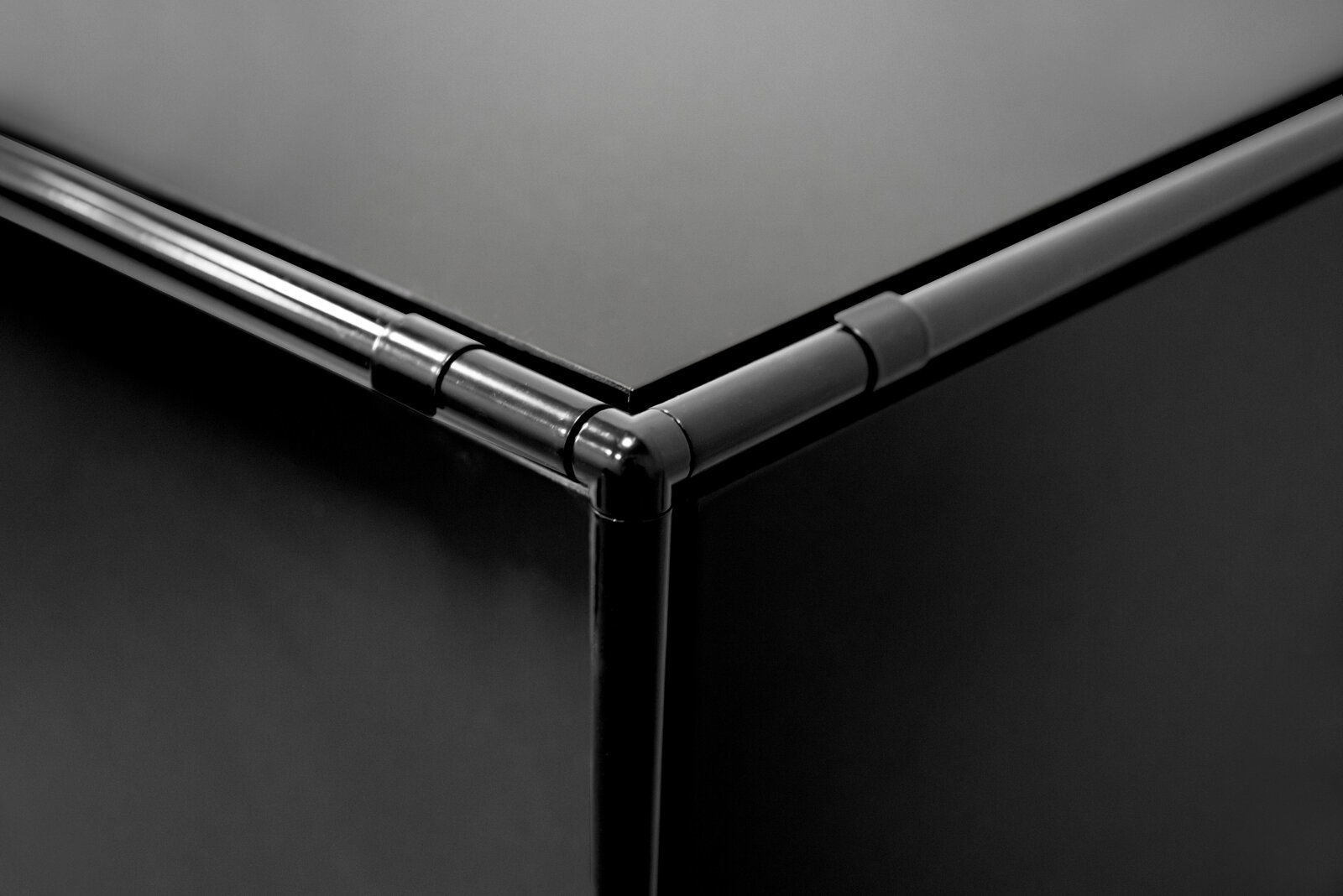 Nahaufnahme einer Ecke eines schwarzen Highboards mit Metallrahmen, aus der Vogelperspektive fotografiert.