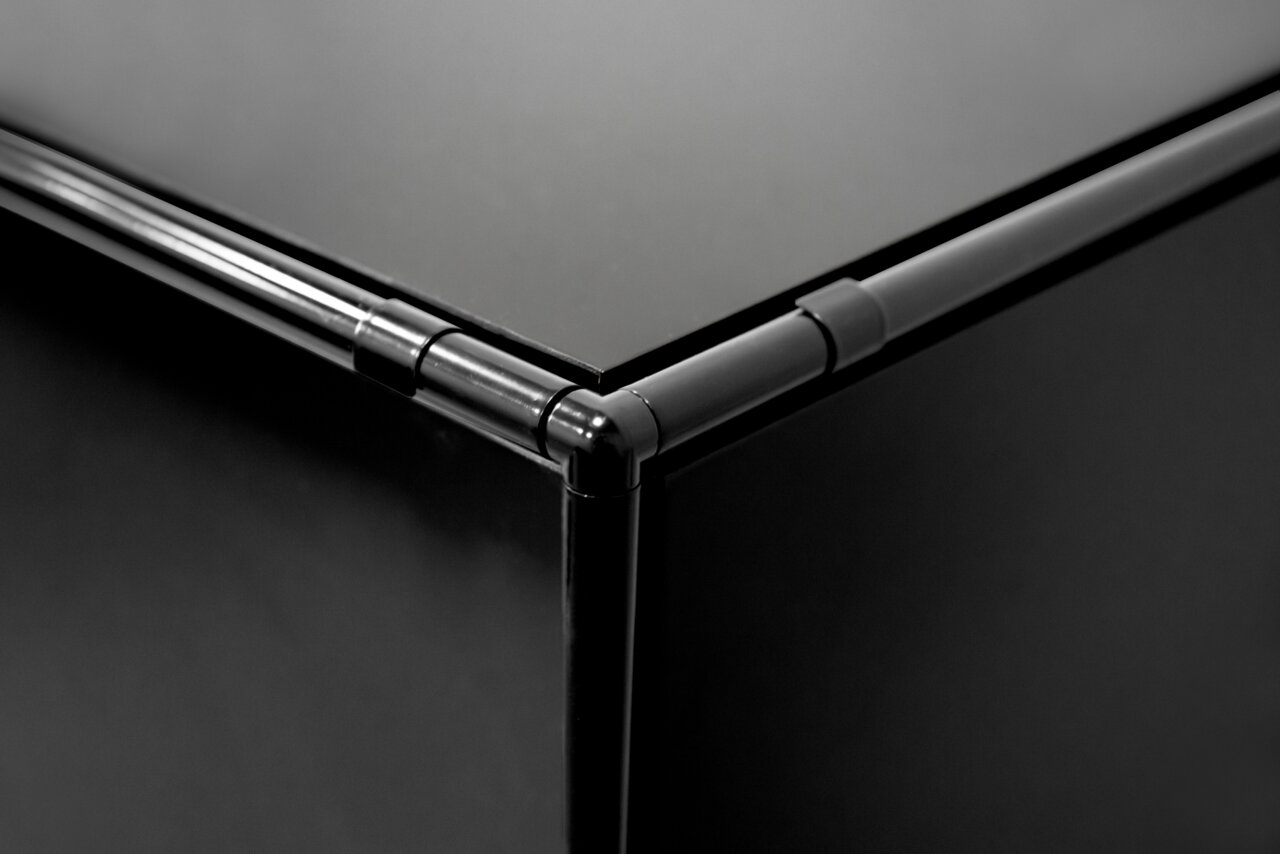 Nahaufnahme einer Ecke eines schwarzen Highboards mit Metallrahmen, aus der Vogelperspektive fotografiert.