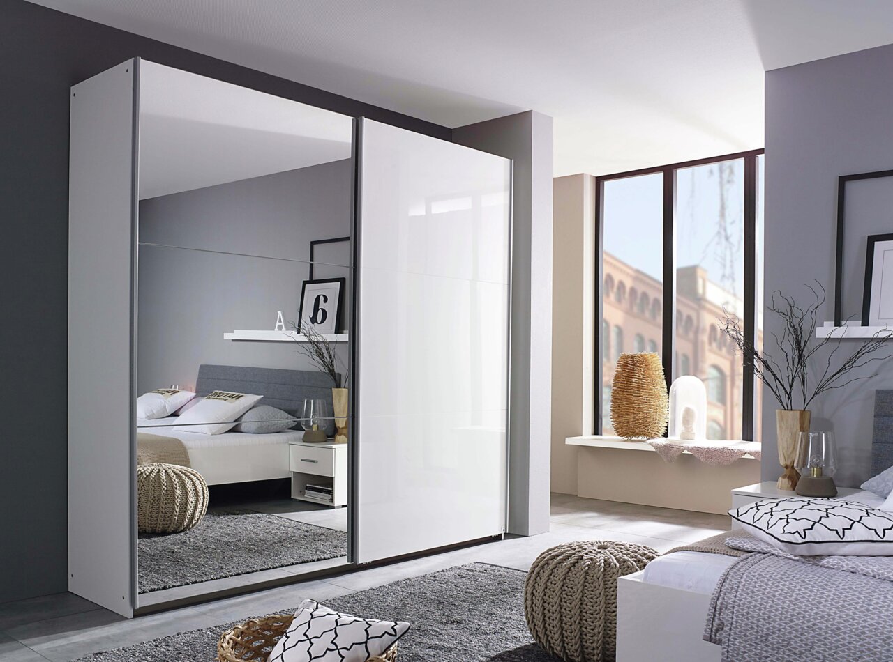 Moderner Schwebetürenschrank mit zwei Türen, eine davon mit Spiegel, in einem stilvoll eingerichteten Schlafzimmer. Perspektive von schräg vorne.