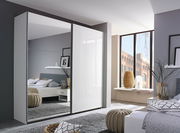 Moderner Schwebetürenschrank mit zwei Türen, eine davon mit Spiegel, in einem stilvoll eingerichteten Schlafzimmer. Perspektive von schräg vorne.