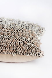 Nahaufnahme eines dekorativen Kissens mit strukturierter, mehrfarbiger Oberfläche in Beige- und Brauntönen, seitliche Perspektive.