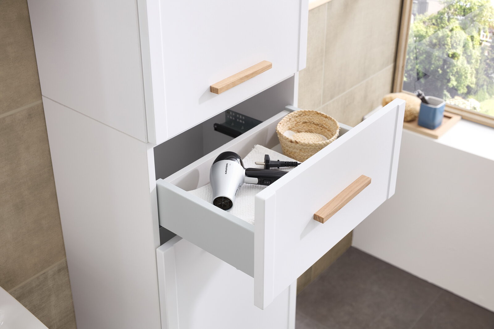 Hochschrank mit geöffneter Schublade, die einen Föhn und einen Korb zeigt, seitliche Perspektive
