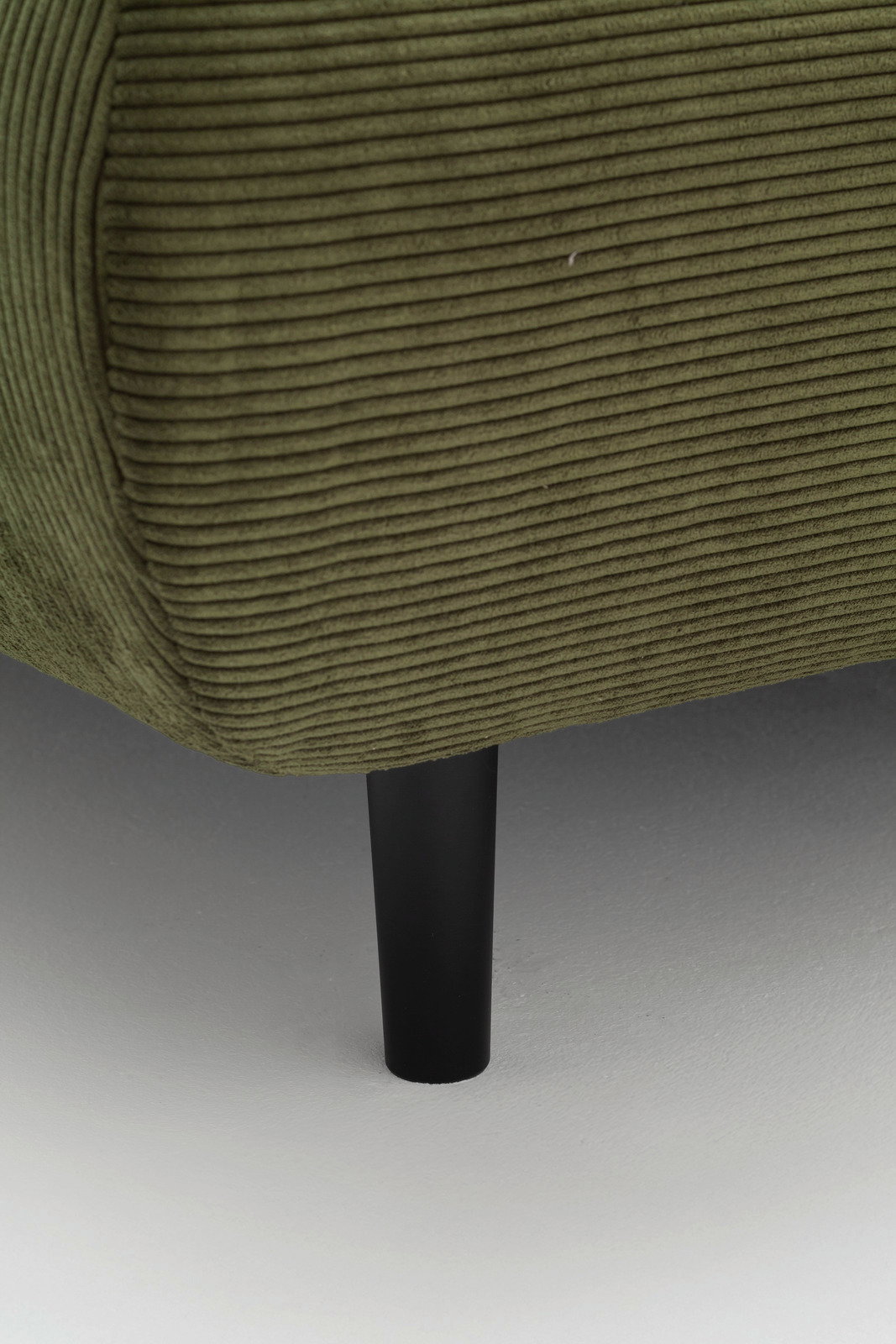 Nahaufnahme eines grünen, gerippten Sofas mit schwarzem Bein, seitliche Perspektive.