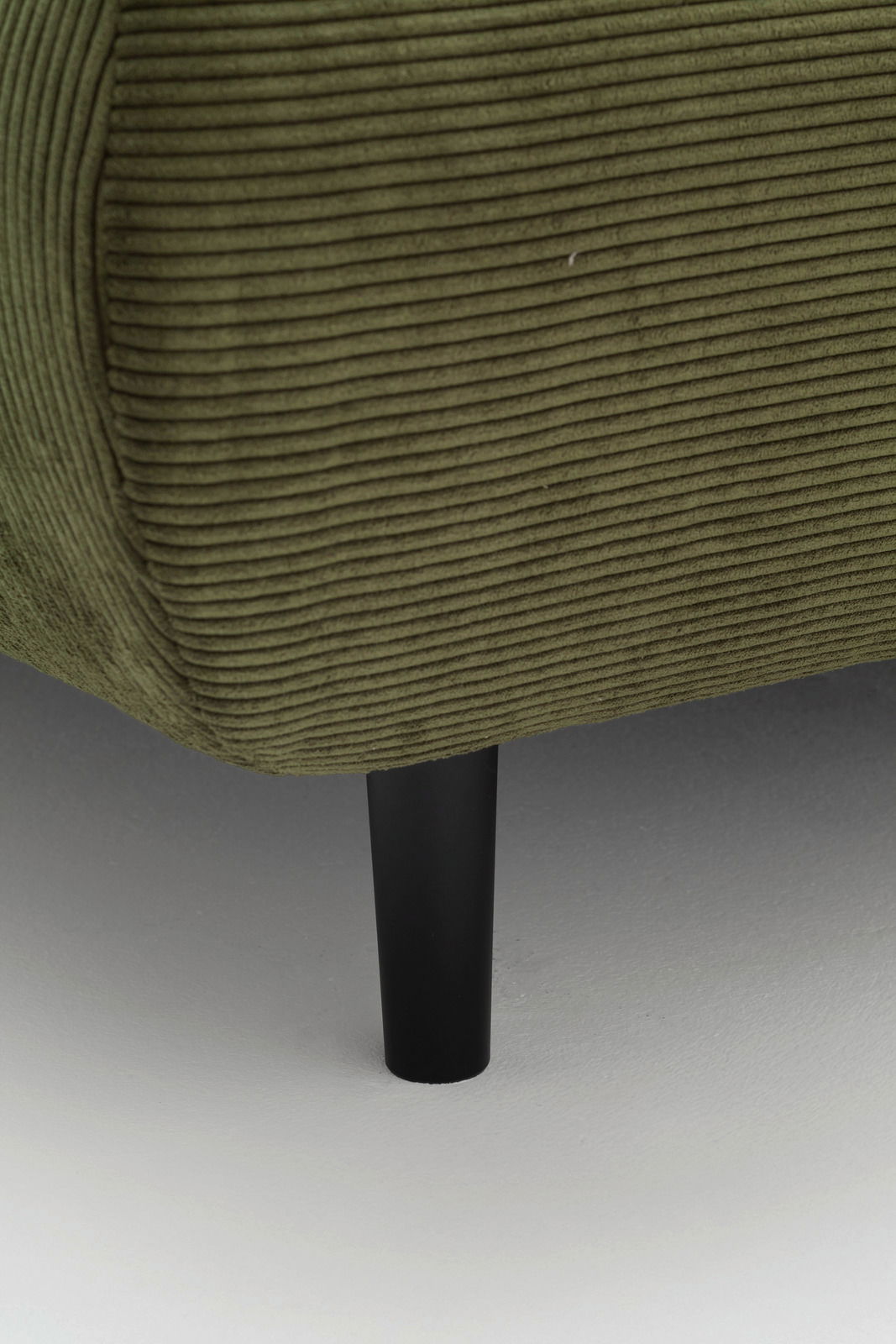 Nahaufnahme eines grünen, gerippten Sofas mit schwarzem Bein, seitliche Perspektive.