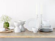 Weißes Porzellan-Geschirrset mit Tassen, Tellern und Untertassen auf Holztisch dekoriert mit Kerzenständern und Vase, frontal in leichter Schrägansicht