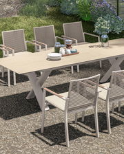 Garten Ausziehtisch mit sechs Stühlen, gedeckt mit Geschirr und Blumen, aus seitlicher Perspektive fotografiert.
