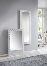 Zwei rechteckige Spiegel mit dekorativem Rahmen, einer stehend an der Wand und der andere an die Wand gelehnt, in einem modernen, hellen Raum mit Teppich und Fenster im Hintergrund.