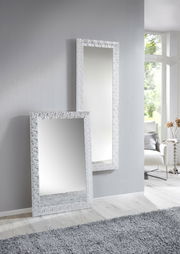 Zwei rechteckige Spiegel mit dekorativem Rahmen, einer stehend an der Wand und der andere an die Wand gelehnt, in einem modernen, hellen Raum mit Teppich und Fenster im Hintergrund.