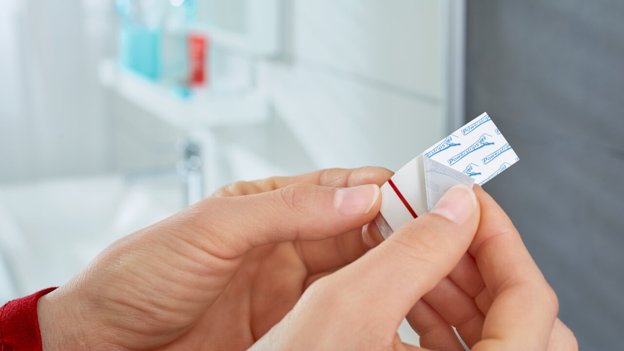 Nahaufnahme von Händen, die einen tesa Powerstrip Waterproof R in einem Badezimmer halten.