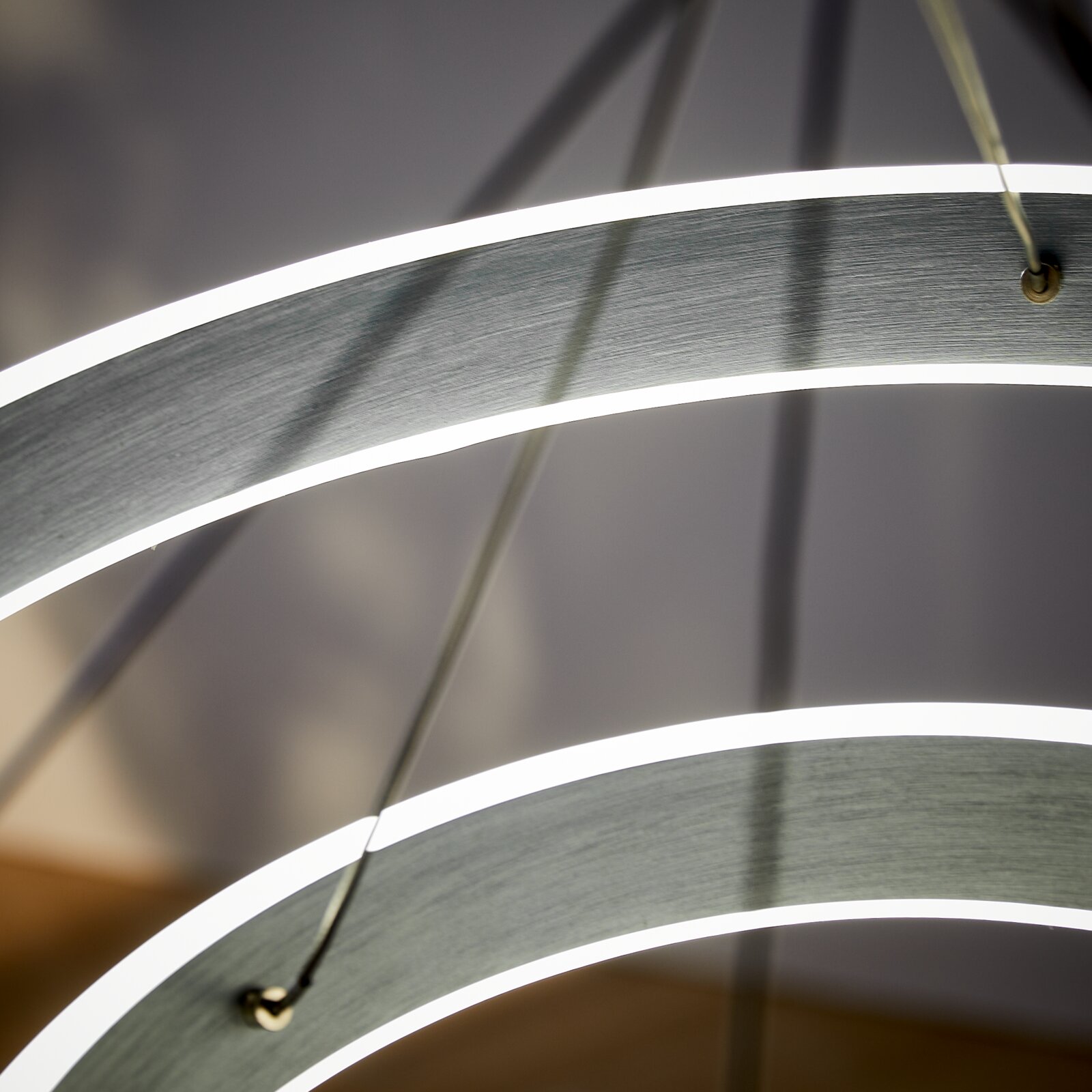 Nahaufnahme einer modernen LED-Hängeleuchte mit geschwungenen, leuchtenden Ringen aus seitlicher Perspektive.