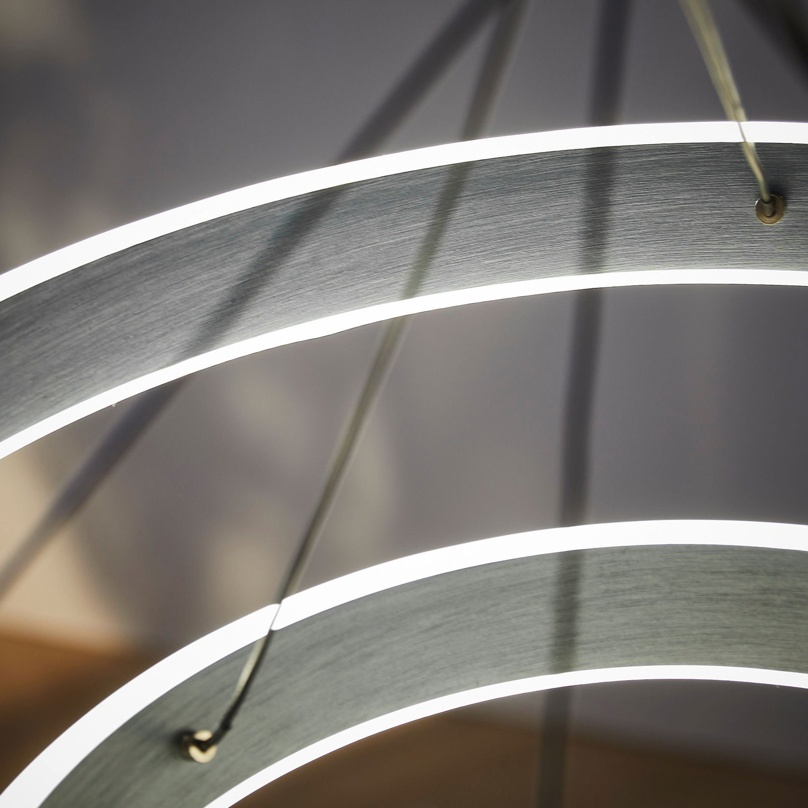 Nahaufnahme einer modernen LED-Hängeleuchte mit geschwungenen, leuchtenden Ringen aus seitlicher Perspektive.