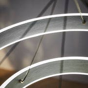 Nahaufnahme einer modernen LED-Hängeleuchte mit geschwungenen, leuchtenden Ringen aus seitlicher Perspektive.