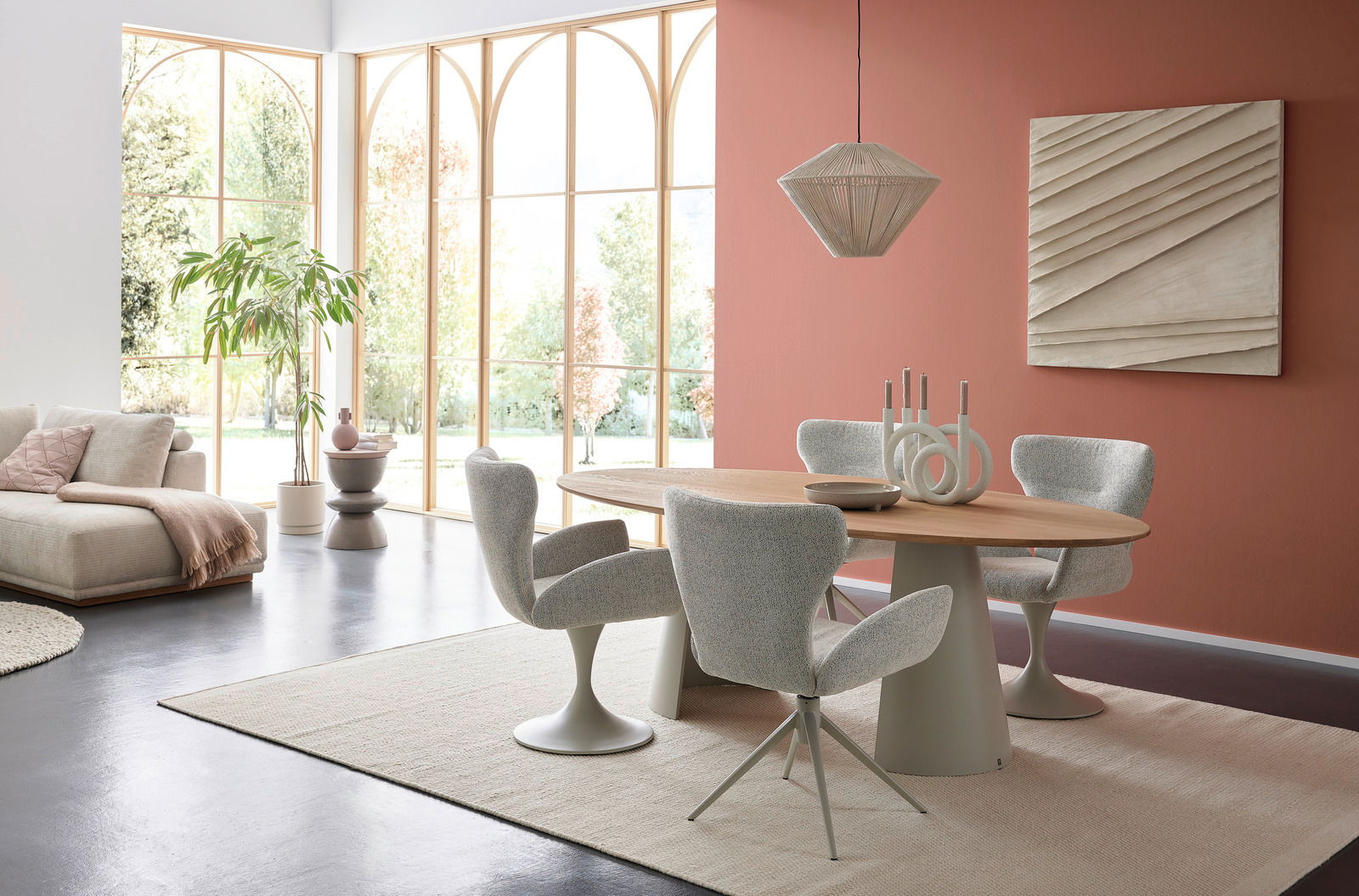 Musterring Esstisch MR JUSTB! Moderner Essbereich mit ovalem Esstisch und vier gepolsterten Armlehnstühlen in einem hellen Raum mit großen Fenstern. Perspektive von der Seite.