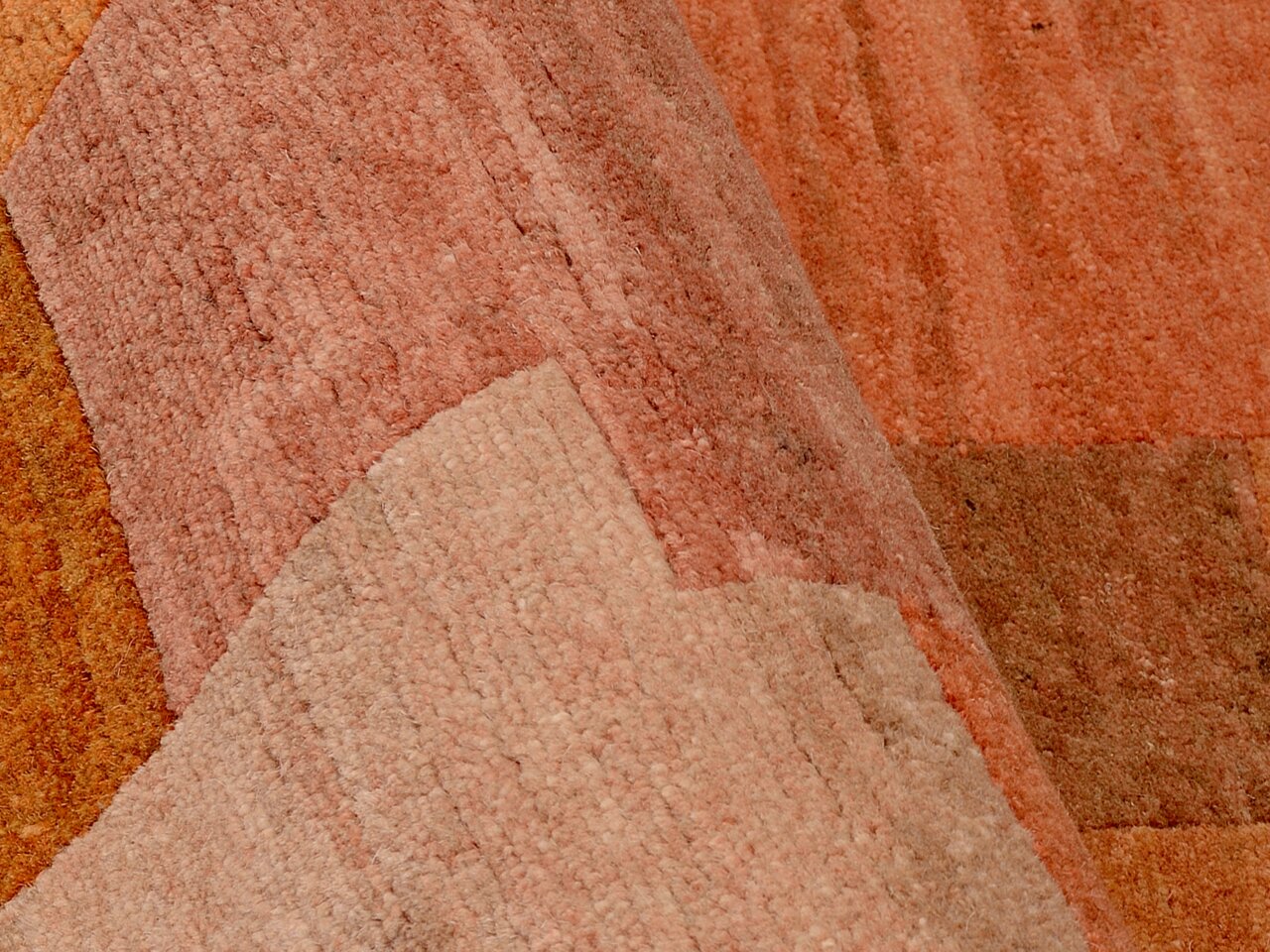 Nahaufnahme eines Wollteppichs in warmen Erdtönen mit geometrischem Muster, von der Seite betrachtet.