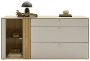 Modernes Sideboard aus hellem Holz mit grauen Schubladen und linker Glastür-Vitrine, dekoriert mit schwarzer Tischlampe, Holzobjekt und Büchern, Frontansicht auf weißem Hintergrund