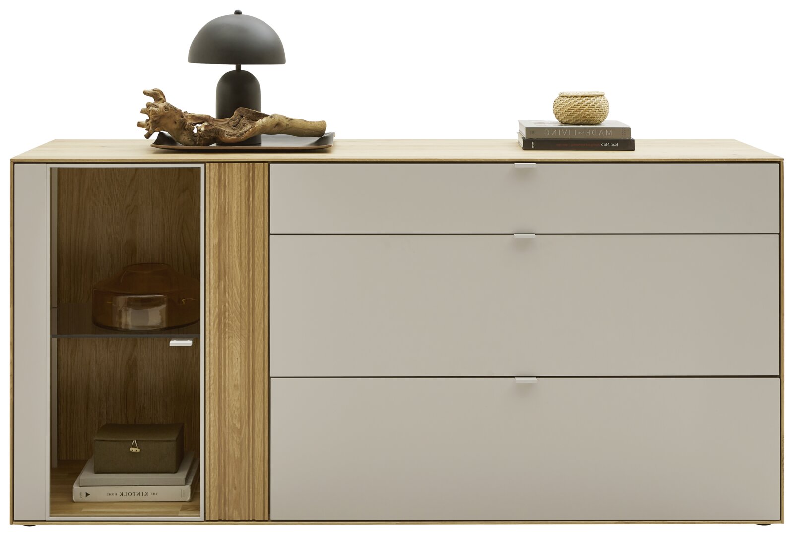 Modernes Sideboard aus hellem Holz mit grauen Schubladen und linker Glastür-Vitrine, dekoriert mit schwarzer Tischlampe, Holzobjekt und Büchern, Frontansicht auf weißem Hintergrund