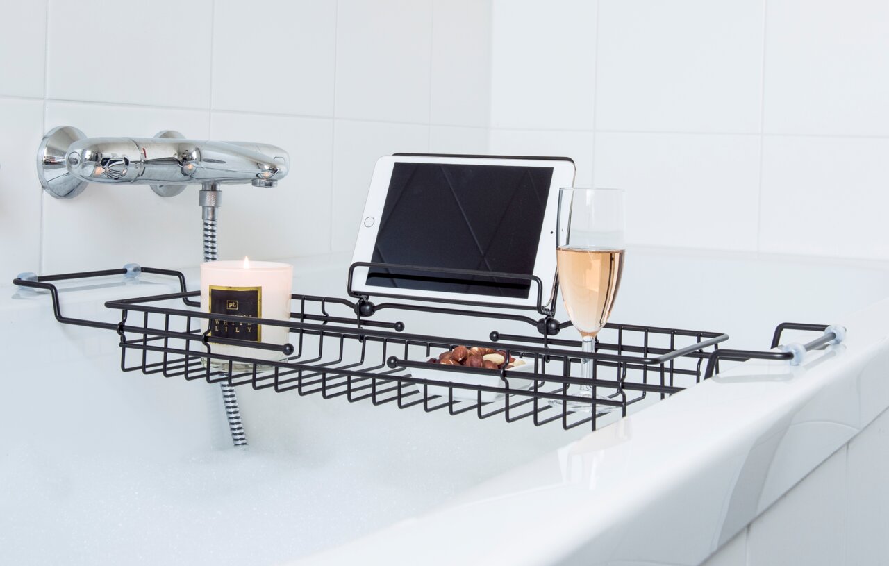 Badablage aus Metall über einer Badewanne, mit Tablet, Kerze, Glas Sekt und Nüssen, seitliche Perspektive