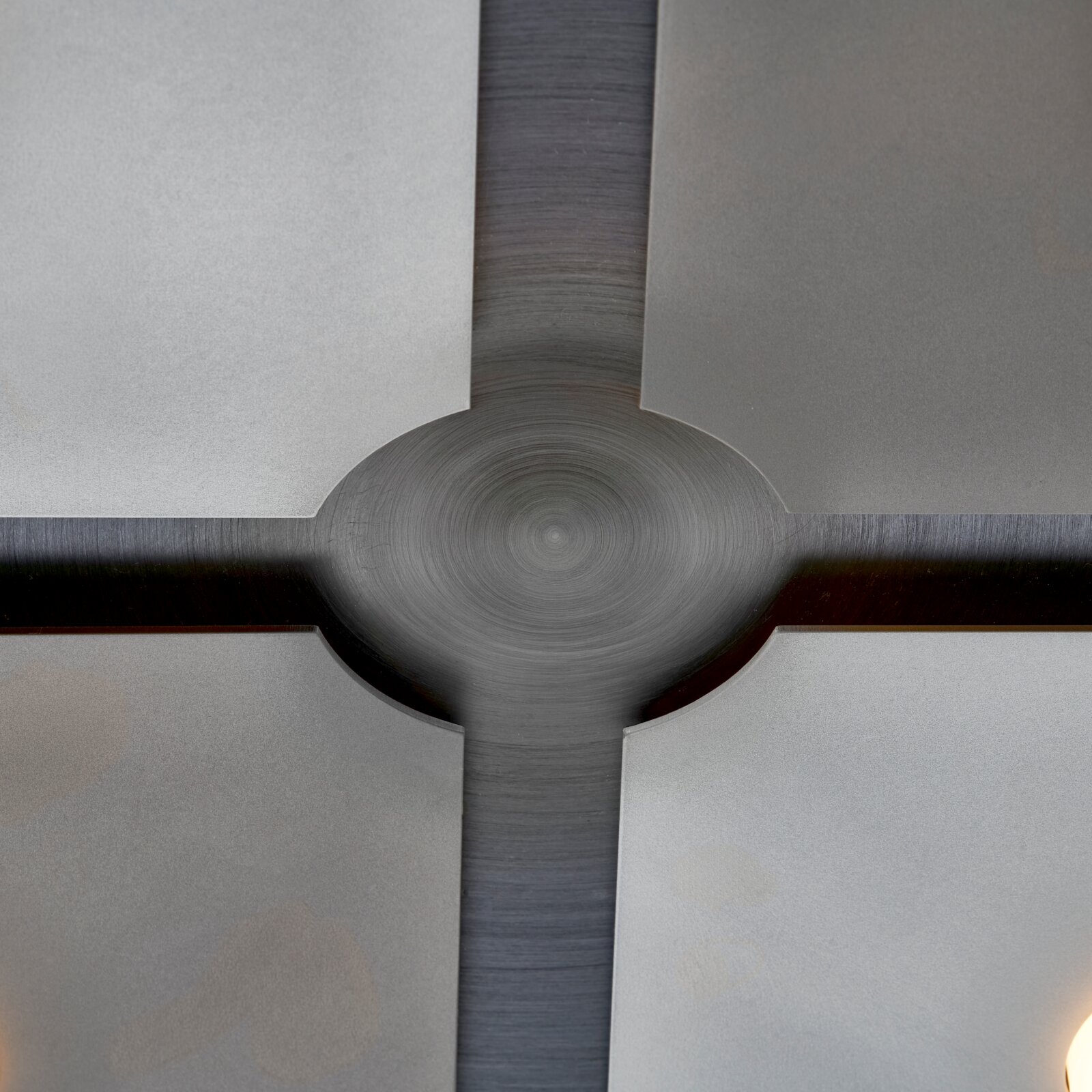 Detailansicht einer modernen Deckenleuchte aus der Untersicht mit gebürstetem Metallkreuz, rundem Zentrum und vier satinierten Glasflächen