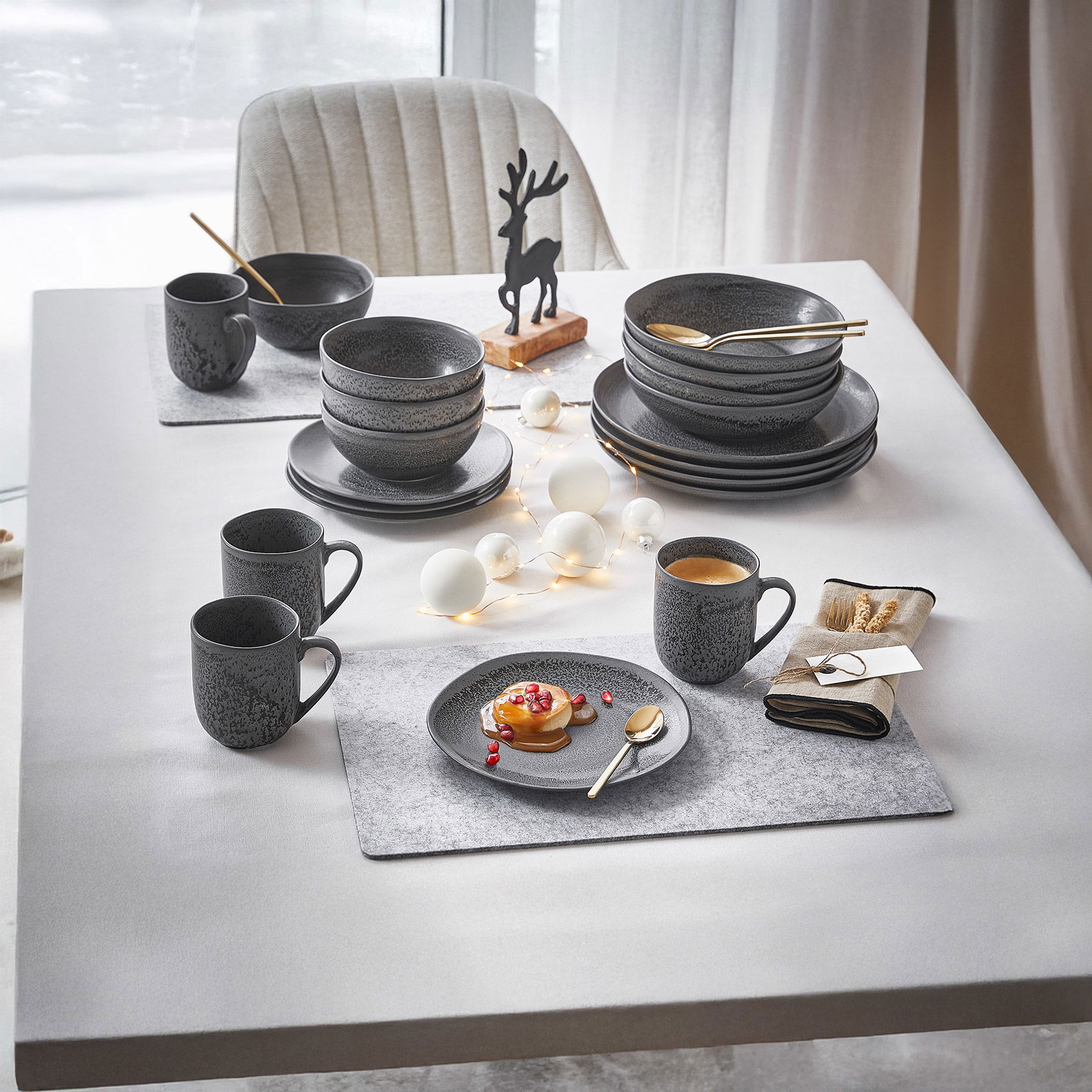 Festlich gedeckter Tisch mit dunkelgrauem Geschirr, Heißgetränken, Deko-Lichtern und kleinem Rentier als winterliche Tischdeko