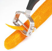 Nahaufnahme eines Sparschälers 'Universale', der eine Karotte schält, mit Fokus auf die Klinge und den Schälvorgang.