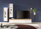 Moderne Wohnzimmer-Vitrine in Weiß und Holzoptik, frontal betrachtet, mit dekorativen Objekten und einem großen Fernseher.
