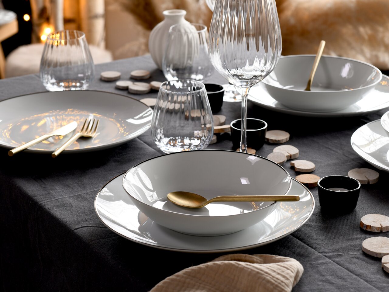 Elegantes Tafelservice Luna Black, 12-teilig, auf einem festlich gedeckten Tisch mit goldfarbenem Besteck und stilvollen Gläsern, seitliche Perspektive.