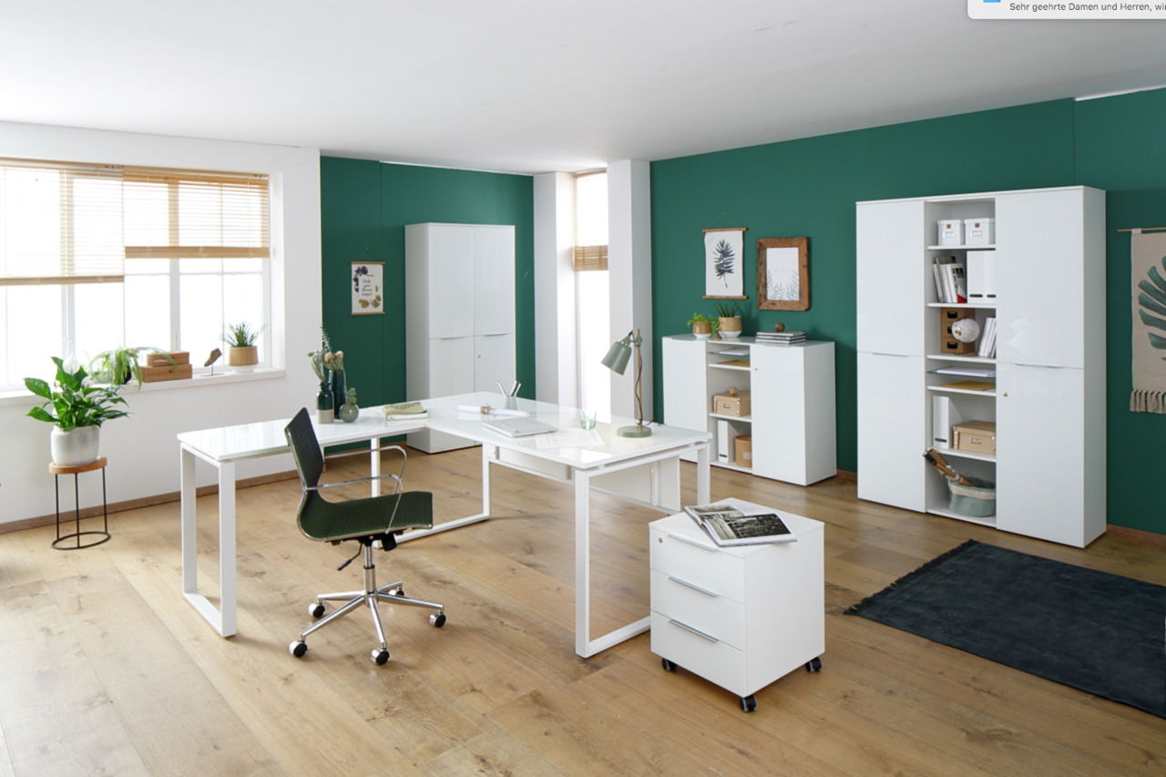 Moderne Büromöbelkombination in einem hellen Raum mit grün gestrichener Wand, bestehend aus einem weißen Schreibtisch, Rollcontainer, Aktenschränken und Sideboard. Perspektive: Frontalansicht.