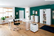 Moderne Büromöbelkombination in einem hellen Raum mit grün gestrichener Wand, bestehend aus einem weißen Schreibtisch, Rollcontainer, Aktenschränken und Sideboard. Perspektive: Frontalansicht.