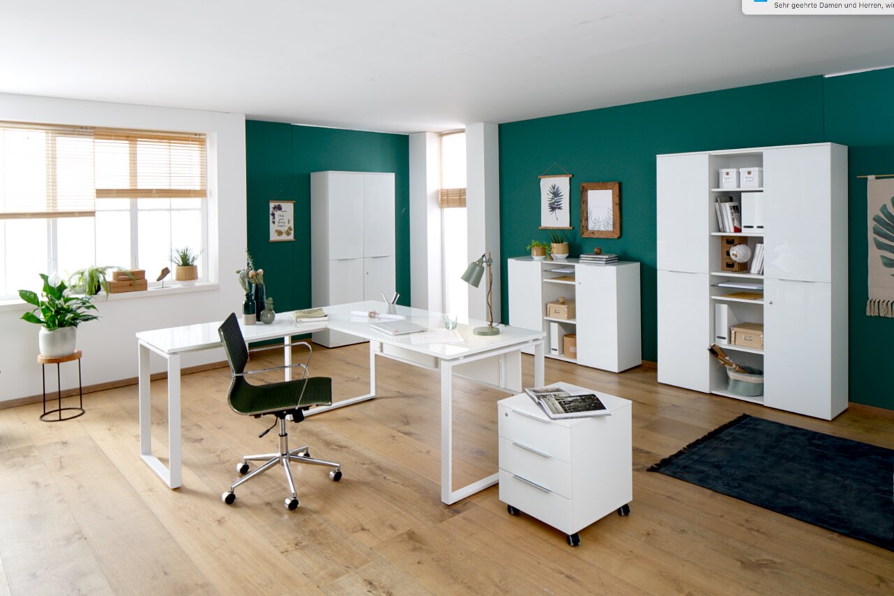 Moderne Büromöbelkombination in einem hellen Raum mit grün gestrichener Wand, bestehend aus einem weißen Schreibtisch, Rollcontainer, Aktenschränken und Sideboard. Perspektive: Frontalansicht.