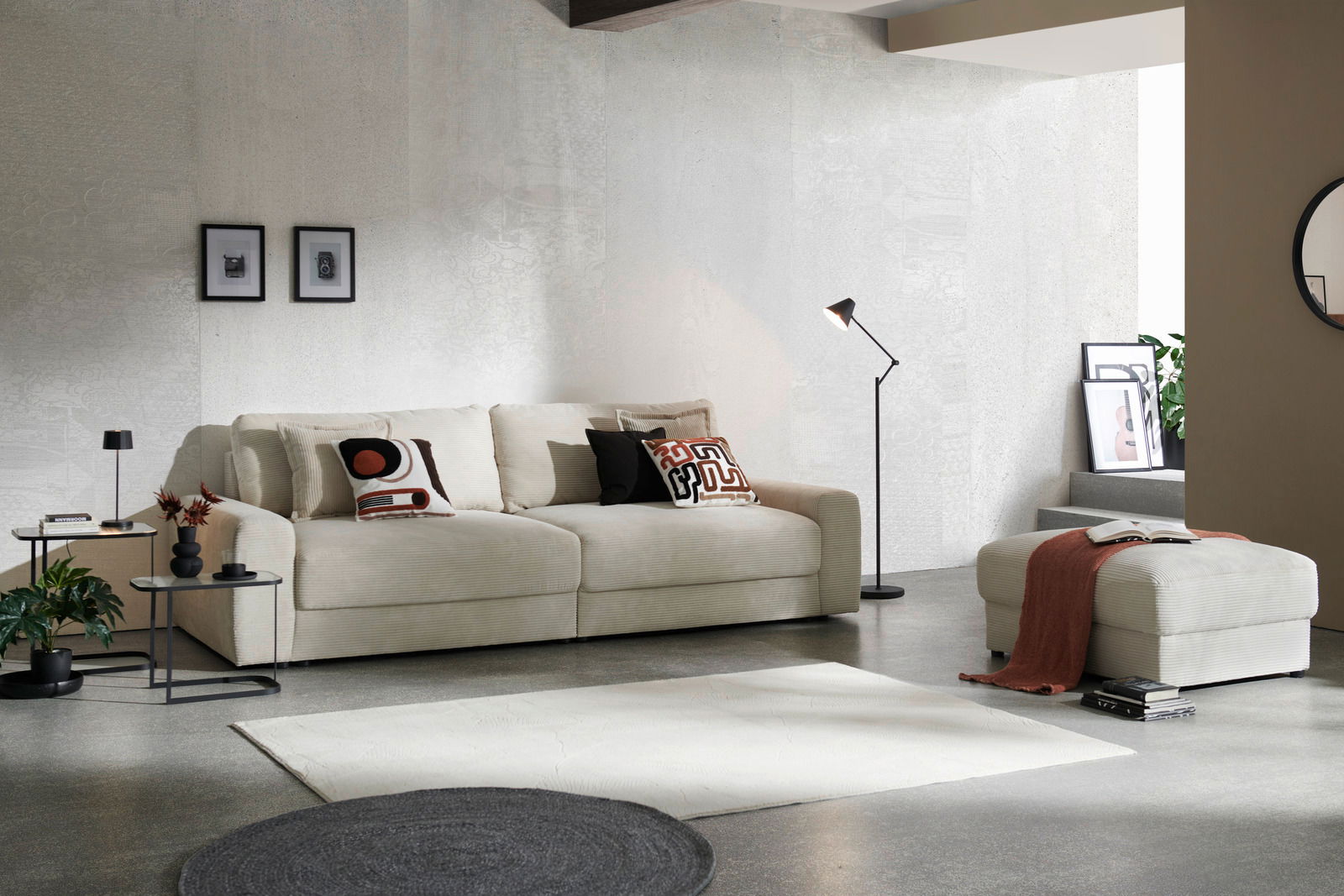 Großes, cremefarbenes Big-Sofa in modernem Wohnzimmer, seitliche Perspektive, mit dekorativen Kissen und passendem Hocker.