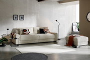 Grote, crèmekleurige bank in een moderne woonkamer, gezien vanaf de zijkant, met sierkussens en een bijpassende poef.