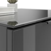 Nahaufnahme einer modernen, glänzenden Nachtkommode in dunkler Farbe mit einer Pflanze und Büchern darauf, aus seitlicher Perspektive.