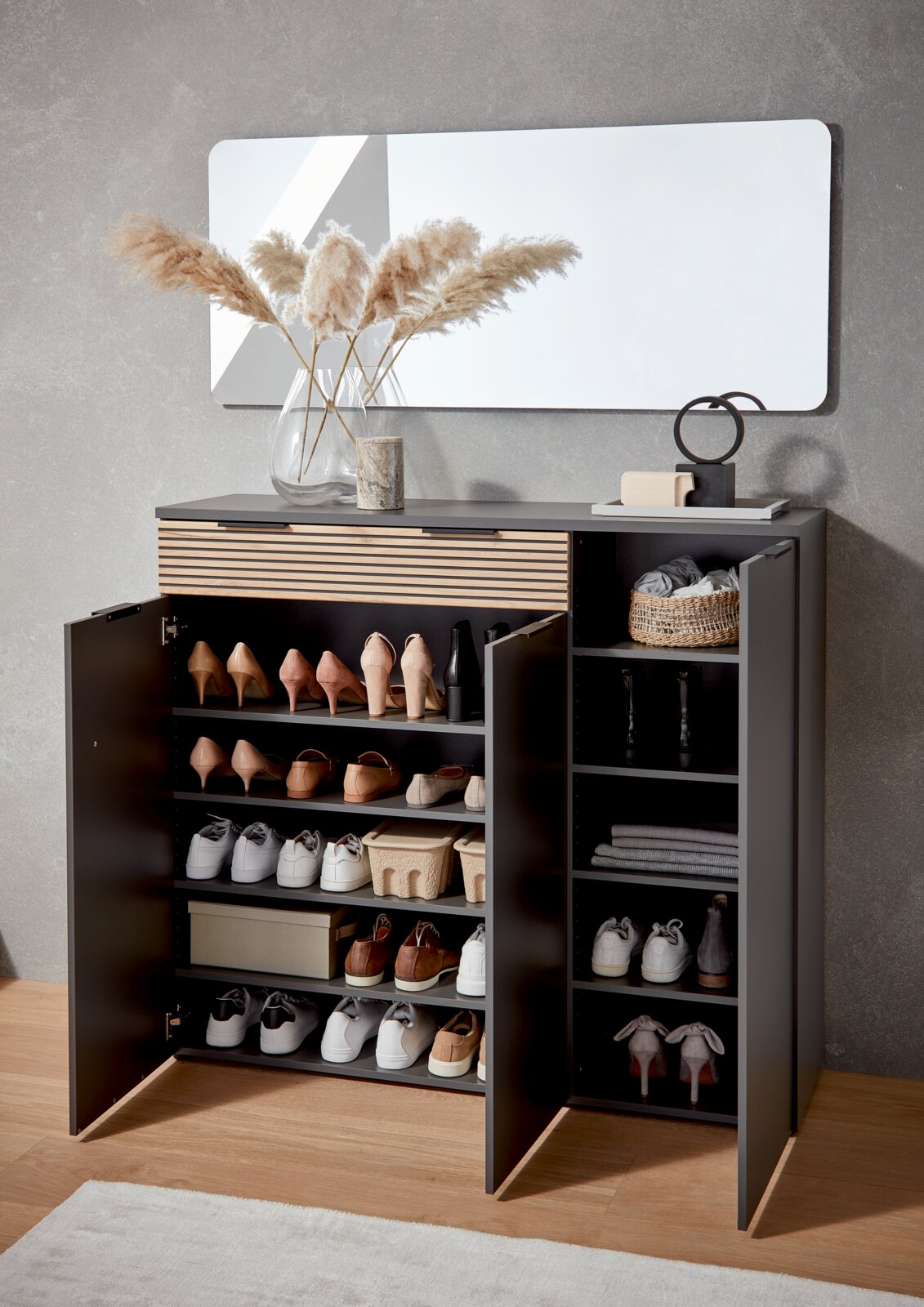 Moderne schwarze Schuhkommode mit Holz-Lamellenfront, geöffnete Türen mit mehreren Schuhfächern und Seitenregal, Frontansicht in leicht schräger Perspektive im Flur unter einem Wandspiegel