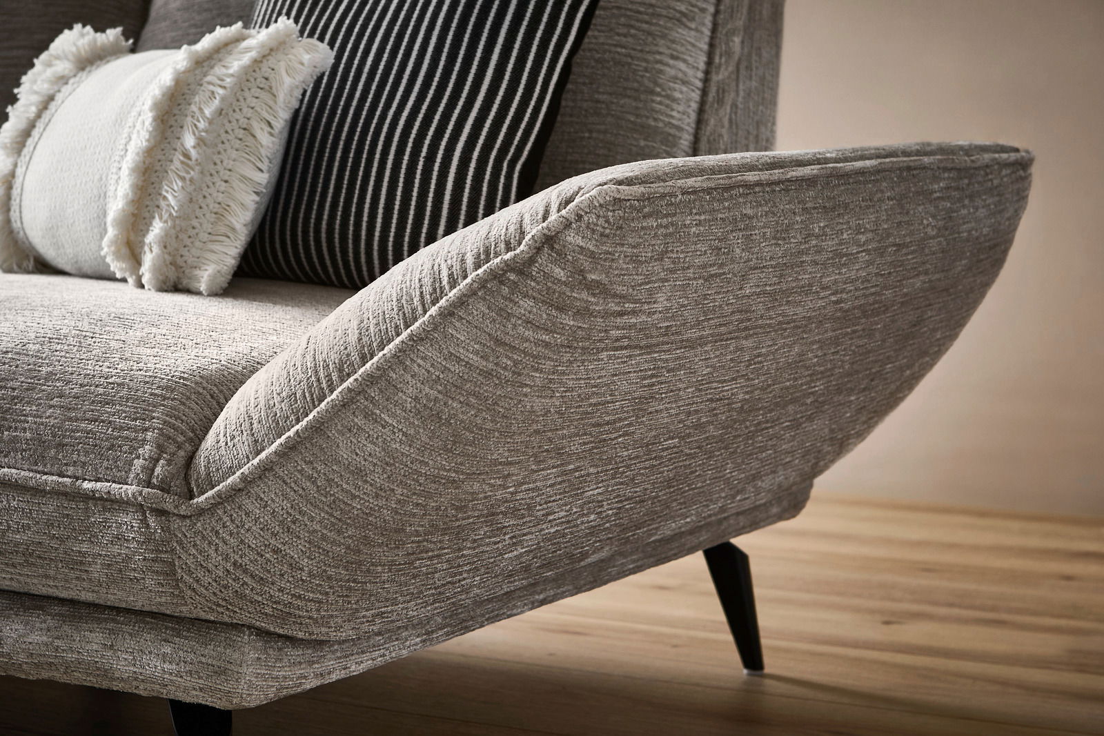 Nahaufnahme eines modernen Longchairs mit grauem Stoffbezug und dekorativen Kissen, seitliche Perspektive.