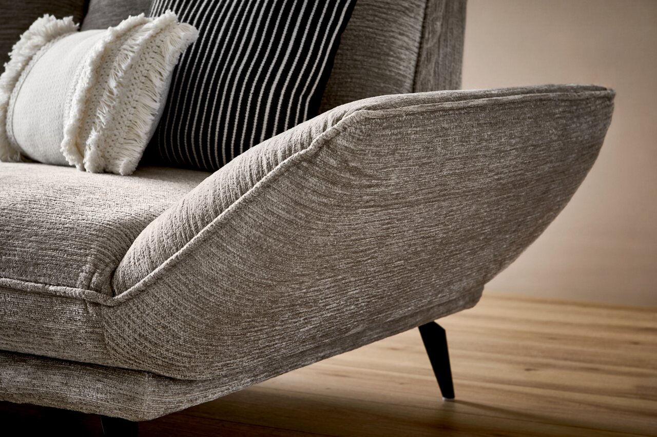 Nahaufnahme eines modernen Longchairs mit grauem Stoffbezug und dekorativen Kissen, seitliche Perspektive.