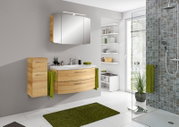 Moderne Badkombination mit Holzoptik, bestehend aus einem Waschtisch mit Schubladen, einem Spiegelschrank und einem hohen Schrank, aus der Perspektive eines hellen Badezimmers mit grünen Akzenten.