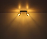 Zweiflammiger Strahler aus schwarzem Metall, montiert an der Decke, mit warmem Lichtschein, seitliche Perspektive.