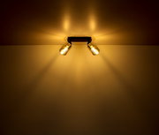 Zweiflammiger Strahler aus schwarzem Metall, montiert an der Decke, mit warmem Lichtschein, seitliche Perspektive.