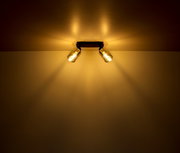 Zweiflammiger Strahler aus schwarzem Metall, montiert an der Decke, mit warmem Lichtschein, seitliche Perspektive.